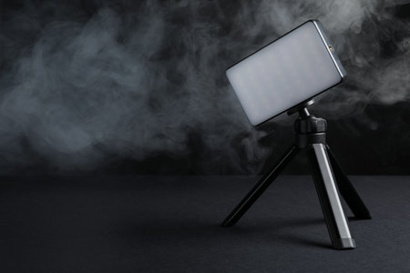 LED lamp on tripod against black background with smoke. Space for textの写真素材