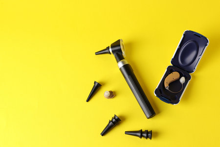 Modern otoscope, hearing aid and ear speculums on yellow background, flat layの写真素材