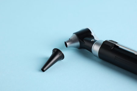 Hearing test. Modern otoscope and ear speculum on light blue background, closeup. Space for textの写真素材