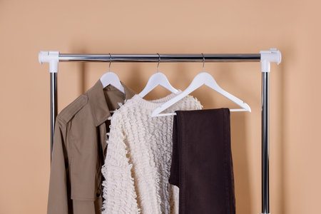 Different stylish clothes hanging on rack against beige background, closeupの写真素材