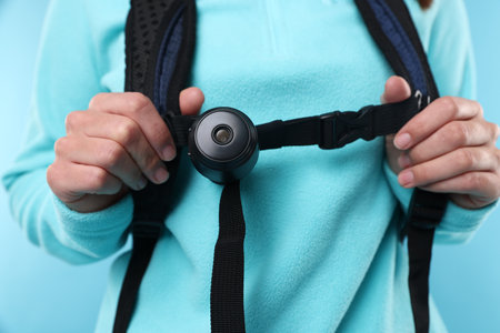 Tourist with camera and backpack on light blue background, closeup
