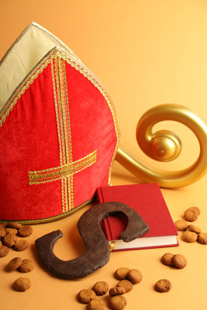 Sinterklaas (Saint Nicholas) Day. Chocolate letter S, kruidnoten cookies, mitre, crosier and notebook on pale orange background, closeupの写真素材