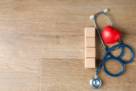 Stethoscope, heart figure and blank cubes on wooden background, flat lay. Mockup for designの写真素材