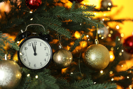 New Year greeting card. Alarm clock, festive lights and shiny baubles on fir tree branches, closeup....