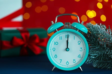 Alarm clock and fir tree branches on blue table against red background with blurred lights, closeup with space for text. New Year greeting cardの写真素材