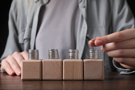 Woman stacking coins and cubes at wooden table, closeupの写真素材