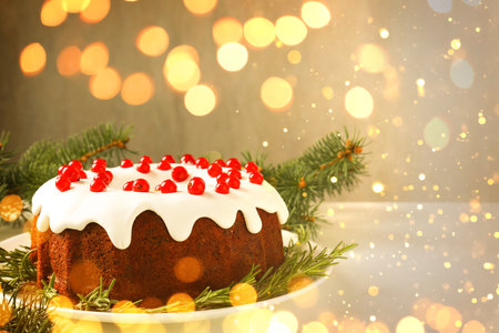 Tasty Christmas cake with red currents and fir branches on table. Bokeh lights