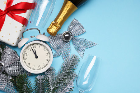 Alarm clock, fir tree branches, bottle of sparkling wine and gift box on light blue background, flat...