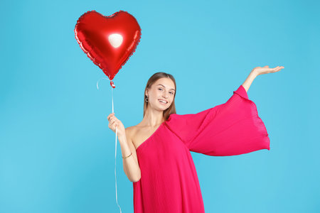 Beautiful woman with heart shaped balloon on light blue background. Romantic giftの写真素材