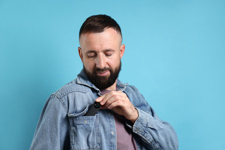 Man with hidden spy camera in his pocket on light blue background