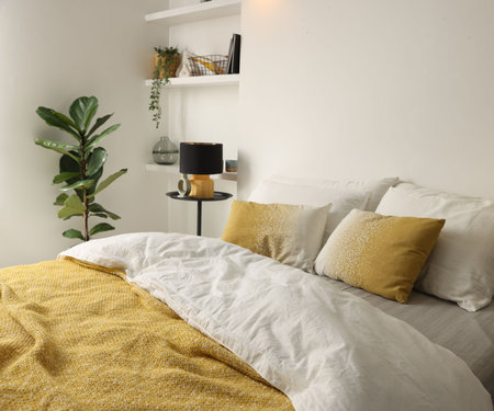 Large bed with linens, bedside table and houseplant near white wall in bedroomの写真素材