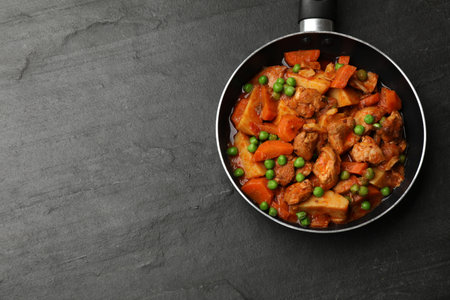 Delicious cooked stew in frying pan and ingredients on black table, top view. Space for textの写真素材