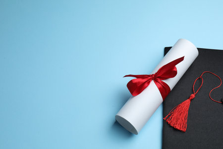 Diploma and graduation hat on light blue background. Space for textの写真素材