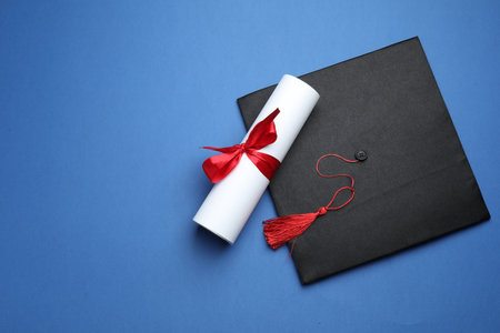 Diploma and graduation hat on blue background, top view. Space for textの写真素材