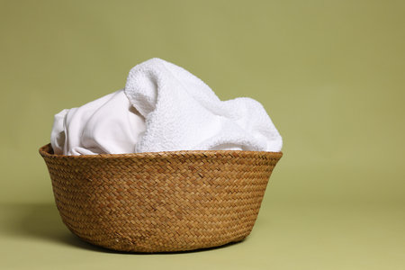 Wicker basket full of laundry against olive background. Space for text