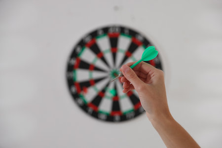Woman with dart aiming at dartboard indoors, selective focusの写真素材