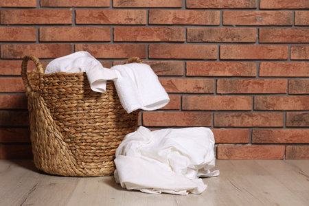 Wicker basket and laundry on floor near brick wall indoors. Space for textの写真素材