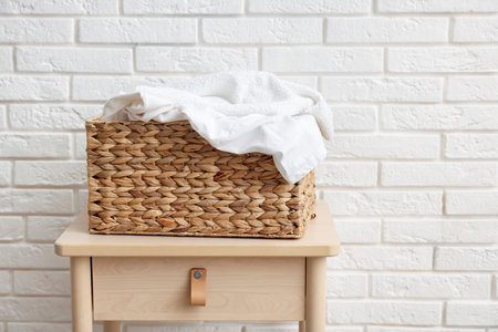 Wicker basket with laundry on table near white brick wall. Space for textの写真素材
