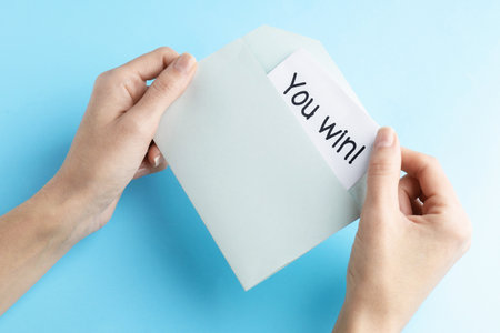 Woman taking card with text You Win! from envelope on light blue background, top viewの写真素材