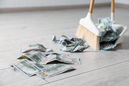 Sweeping dollar banknotes with broom into dustpan on light wooden floor, selective focus. Space for textの写真素材