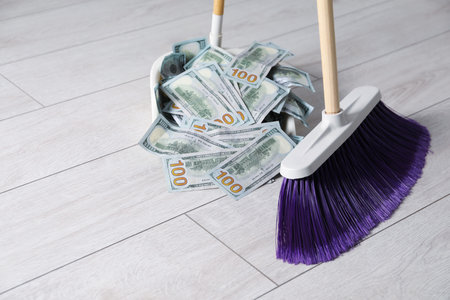 Sweeping dollar banknotes with broom into dustpan on light wooden floor, closeupの写真素材