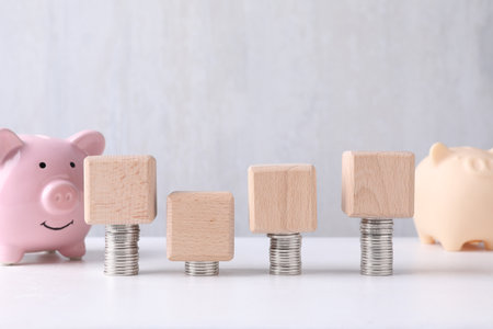 Blank wooden cubes, stacked coins and piggy banks on white table. Mockup for designの写真素材