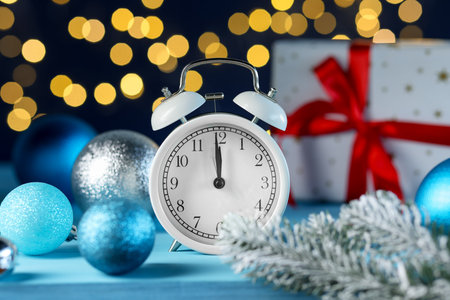 New Year celebration. Alarm clock and festive decor on light blue background against blurred lights, closeupの写真素材