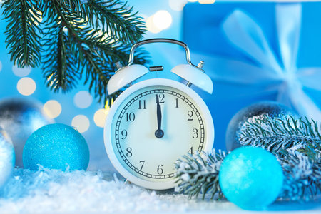 Alarm clock, baubles, fir tree branches and artificial snow on table against light blue background...