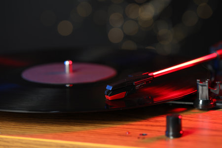 Turntable with vinyl record on background with blurred lights, closeup