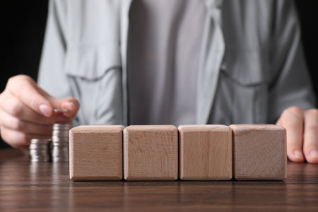 Woman stacking coins at wooden table, focus on blank cubes. Mockup for designの写真素材