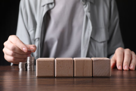 Woman stacking coins at wooden table, focus on blank cubes. Mockup for designの写真素材