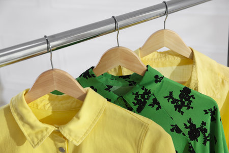 Different stylish clothes hanging on rack near white wall indoors, closeupの写真素材