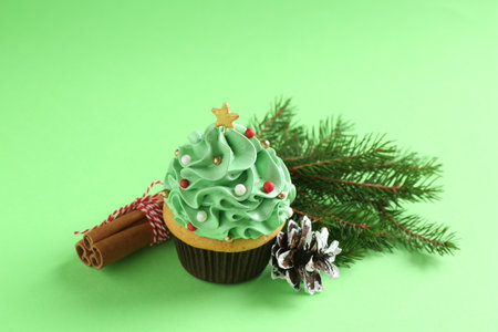 Christmas tree shaped cupcake, cinnamon and festive decor on green background, closeup