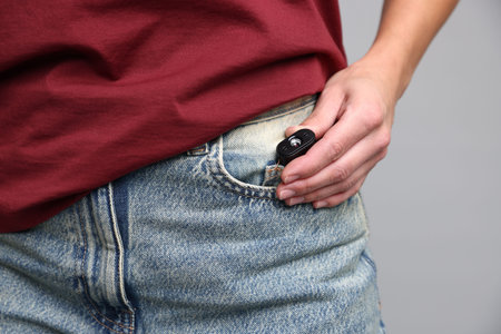 Young woman with hidden spy camera in her pocket on light gray background, closeupの写真素材