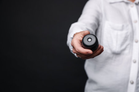 Young woman with hidden camera on black background, closeup. Space for textの写真素材