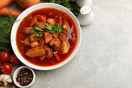 Delicious cooked stew in bowl and fresh ingredients on gray table, flat lay. Space for textの写真素材