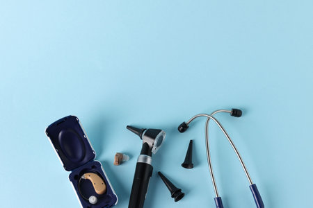 Modern otoscope, hearing aid, stethoscope and ear speculums on light blue background, flat lay. Space for textの写真素材