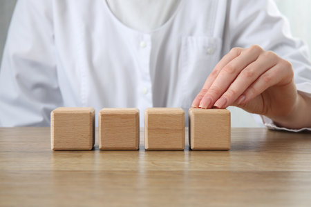 Doctor with blank cubes at wooden table, closeup. Mockup for designの写真素材