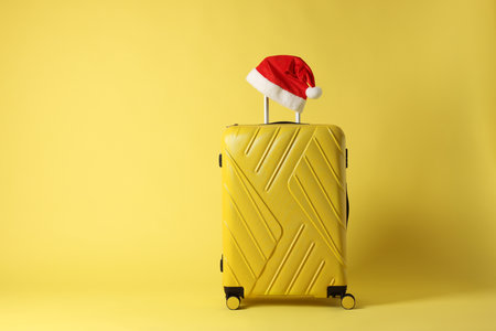 Stylish suitcase with Santa hat on yellow background, space for text. Christmas vacationの写真素材