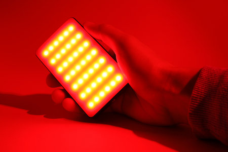 Man holding LED lamp glowing with red light on color background, closeupの写真素材
