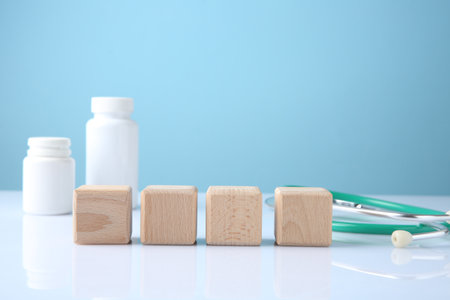 Stethoscope, pills and blank wooden cubes on white table against light blue background. Mockup for designの写真素材