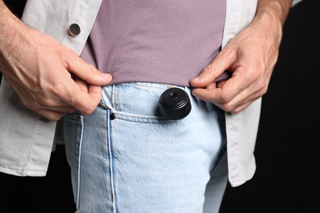 Man with hidden spy camera in his pocket on black background, closeupの写真素材