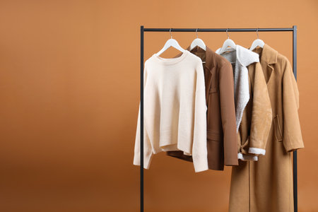 Different clothes hanging on rack against brown background, space for textの写真素材