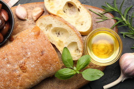 Fresh cut ciabatta, oil, olives, garlic and basil on dark textured table, flat layの写真素材