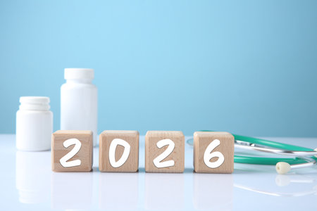 New 2026 year. Cubes with numbers, pills and stethoscope on table against light blue background