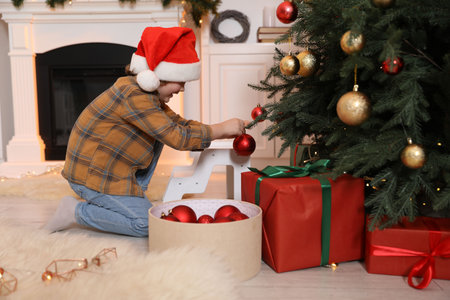 Little boy in Santa hat decorating Christmas tree at homeの写真素材