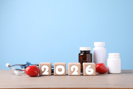 New 2026 year. Cubes with numbers, hearts, pills and stethoscope on table against light blue...