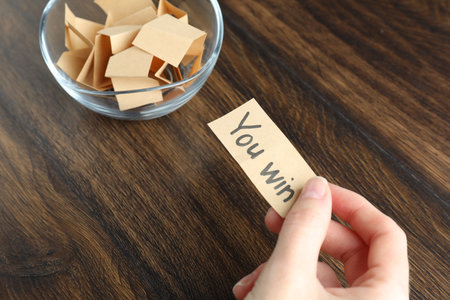 Woman holding note with text You Win and paper pieces at wooden table, above view