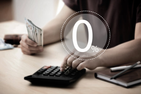 Man with money using calculator at table, closeup. 0 percent representing zero commissionの写真素材