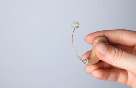 Woman with hearing aid on light gray background, closeup.